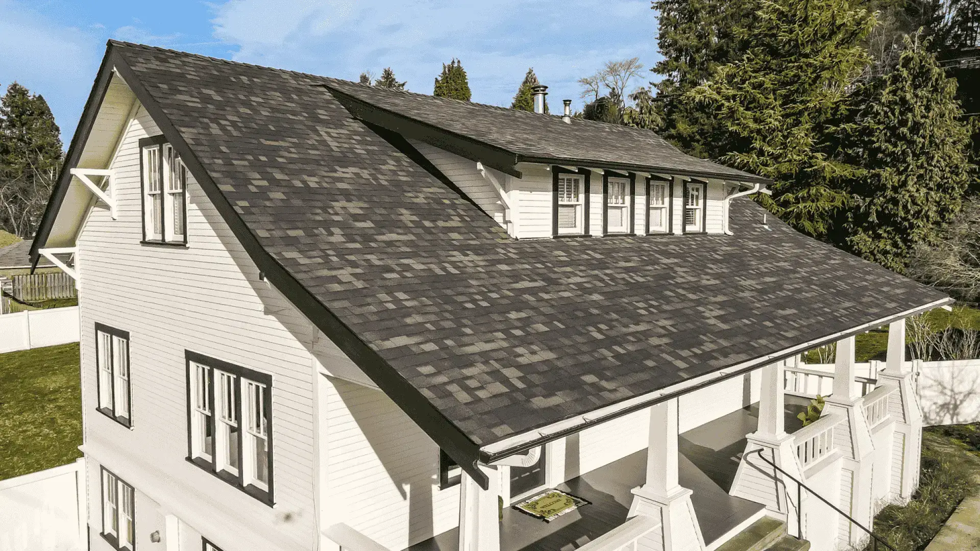 Large white house with dark shingled roof and porch in sunny setting