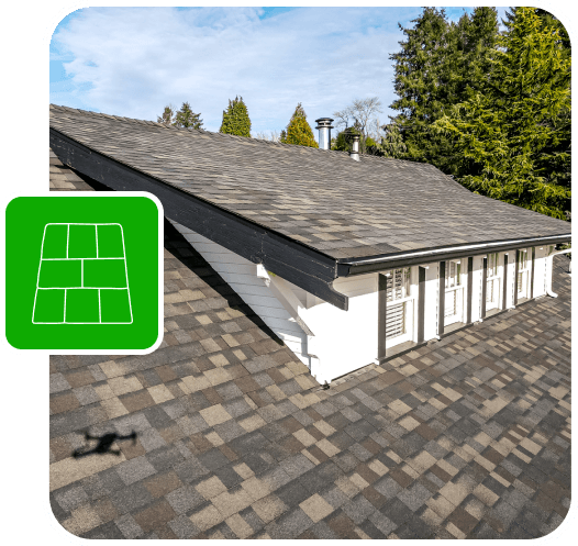 Aerial view of a house roof with asphalt shingles, surrounded by trees.