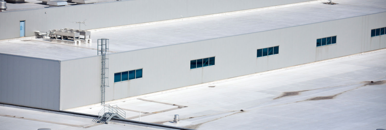 Aerial view of a large industrial building with flat white roof and blue windows.