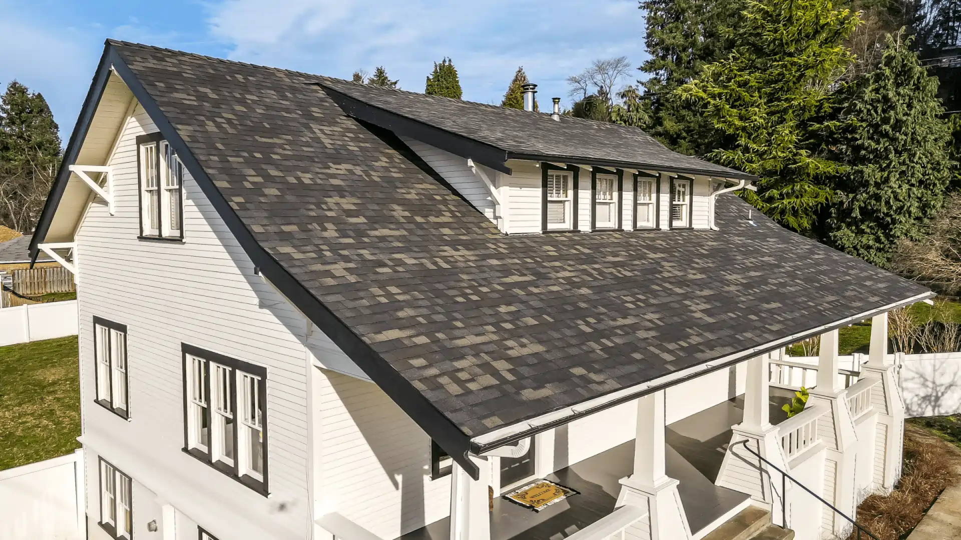 Charming white two-story house with dark shingle roof and surrounding greenery.